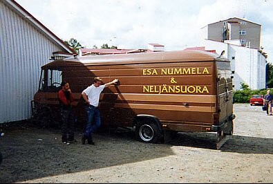 Ruskea pakettiauto, jonka kyljessä lukee Esa Nummela & Neljänsuora, ja sen vieressä kaksi miestä.